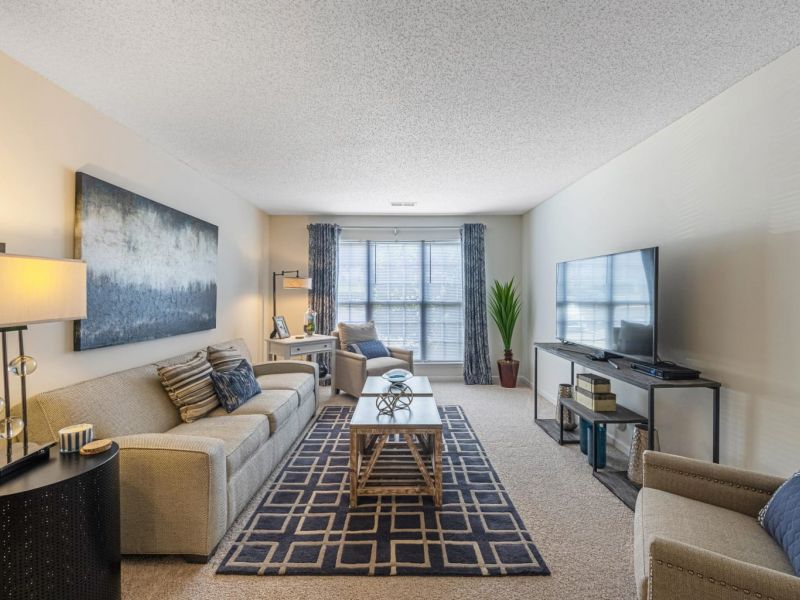 Modern living room with beige furniture, large windows, a TV, and abstract artwork on the wall.