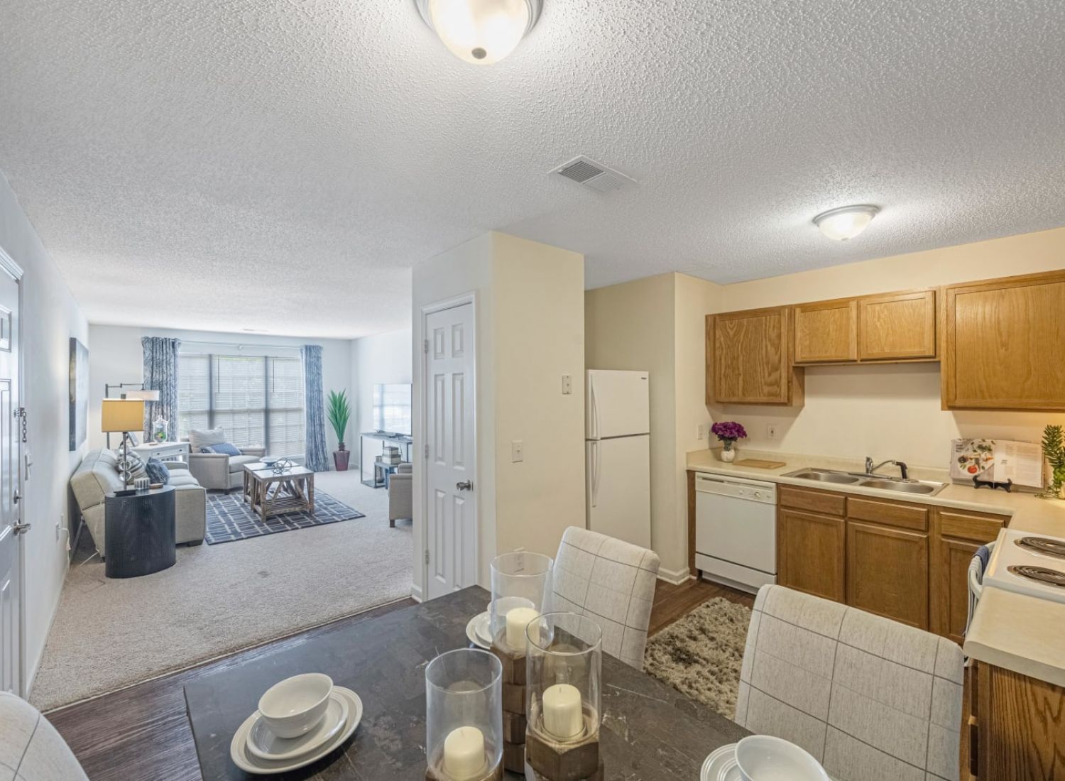 Open kitchen with wood cabinets, dining area set for four, and view of a bright living room with large windows.
