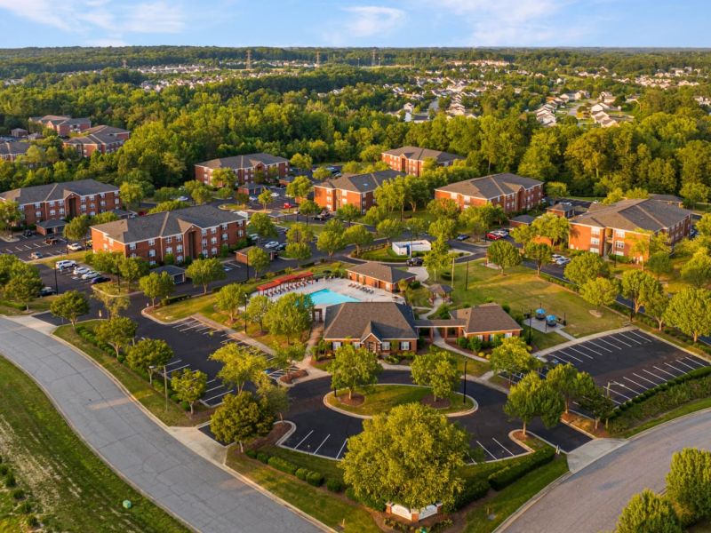 Aerial view of a suburban apartment complex with a central pool, surrounded by trees and parking lots.